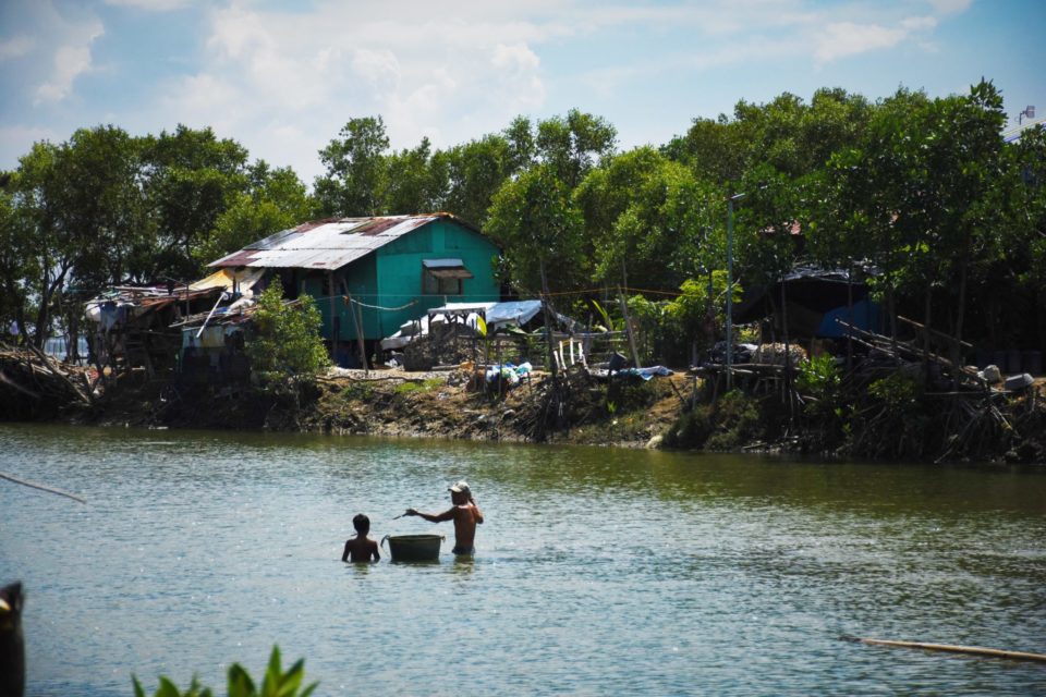 Fish farmer checks the fishing net for any catch while his son tows a plastic pail in which to place the harvested tilapia.